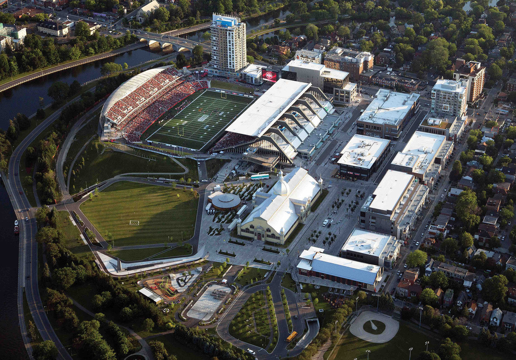 Ariel photo of the fully redeveloped 40 acre Lansdowne Park  - a wide open public green space, the newly rebuilt/refurbished TD Place Stadium, new retail and housing, open public realm elements and farmers market, the historical Aberdeen Pavilion and Historical Building.